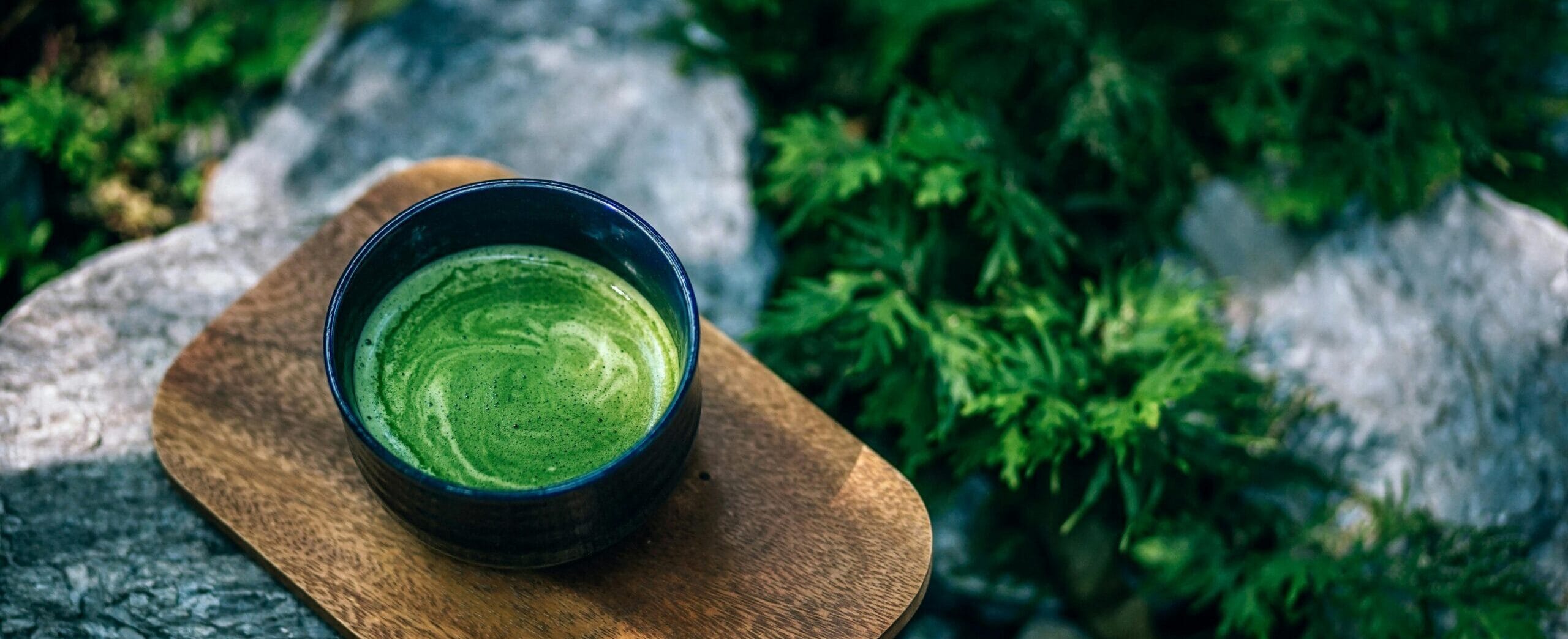 Політика повернення та відшкодування 1 Top view of a green matcha tea served on a wooden tray outdoors, surrounded by rocks.